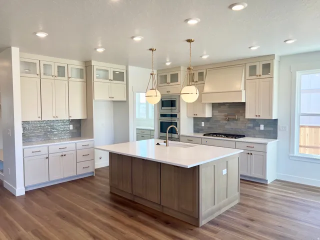 Spacious kitchen featuring an island with a light-toned wood-finish base, ample cabinetry with upper glass-front doors, recessed lighting, and wood-finish flooring