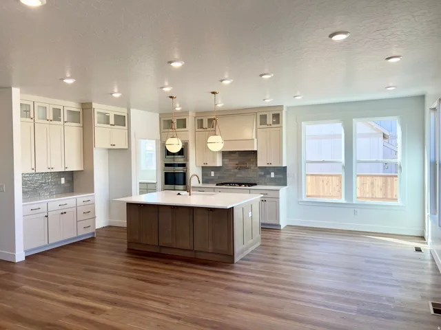 Open-concept kitchen with wood-finish flooring, recessed lighting, a large island with a light-toned countertop, a tile backsplash, and multiple windows