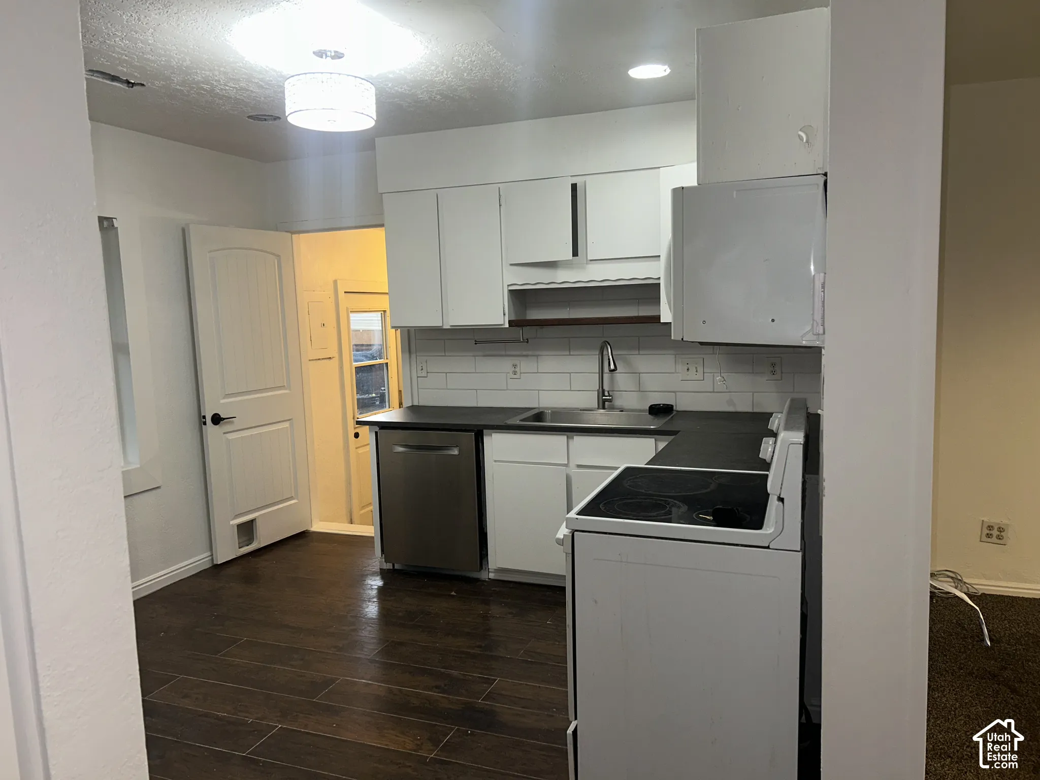 Kitchen featuring white cabinetry, dark countertops, a stainless steel dishwasher, white subway tile backsplash, and wood-finish flooring