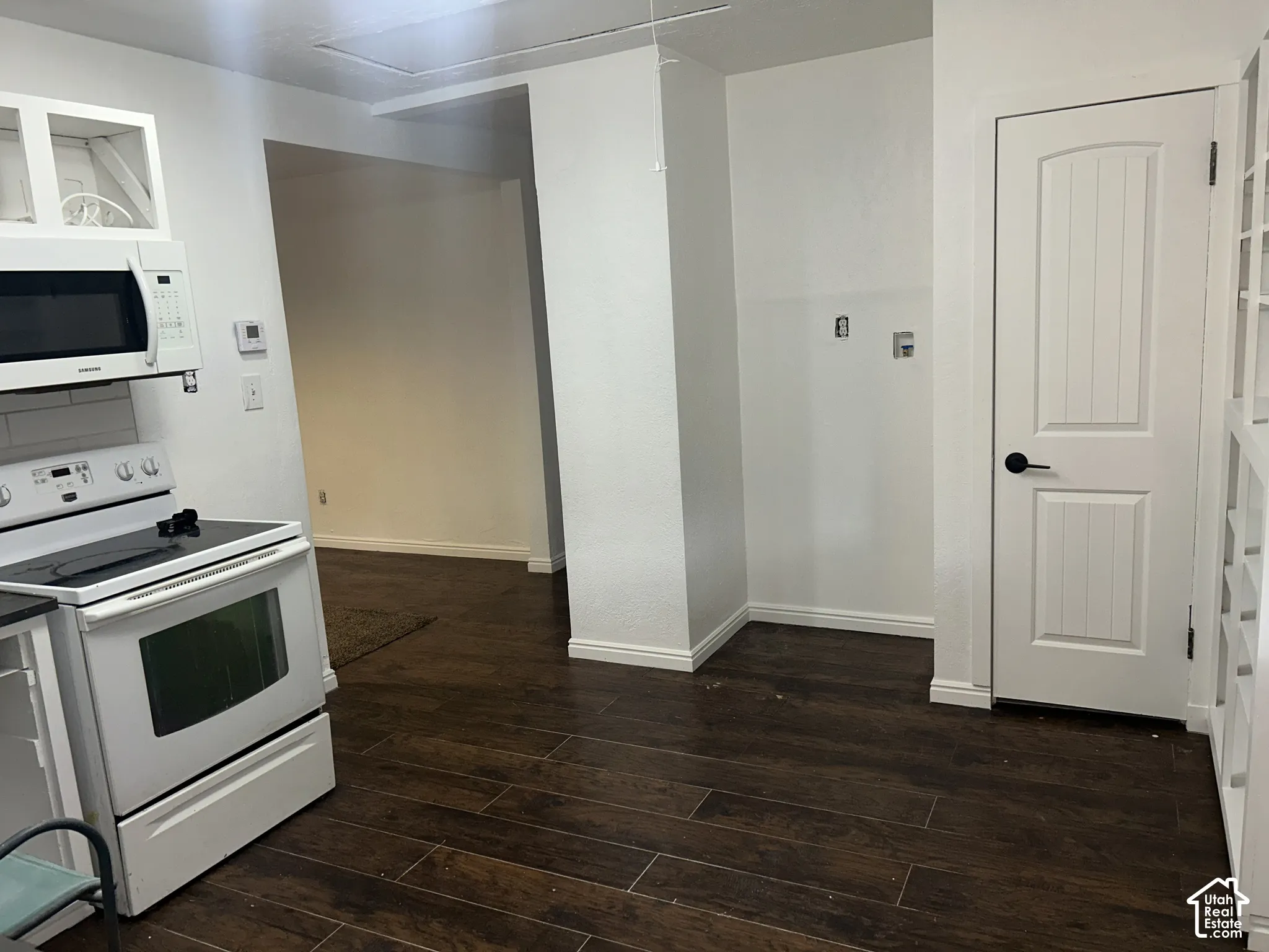 Wood-finish flooring throughout, white overhead cabinetry, and a white electric range with a microwave