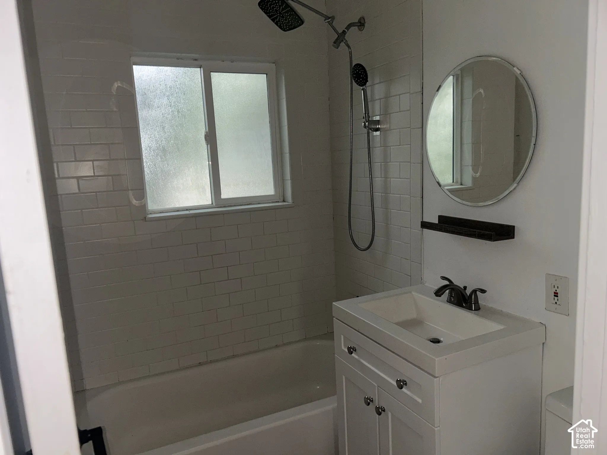 Bathtub with white subway tile surround, matte black rainfall showerhead, and window with frosted glass
