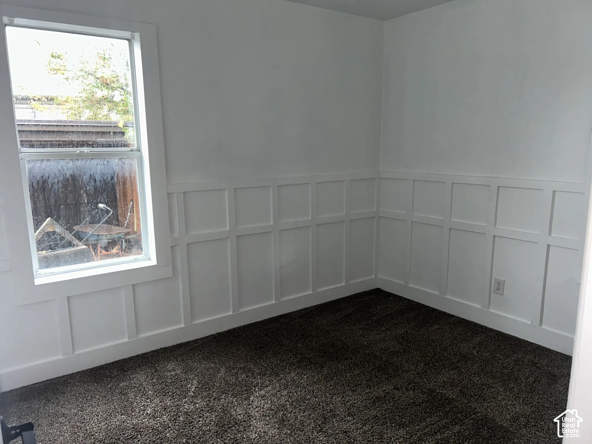 White wall paneling with a double-hung window and dark carpeting