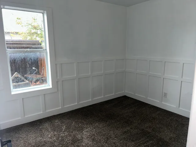 White wall paneling with a double-hung window and dark carpeting