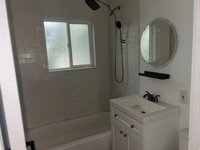 Bathtub with white subway tile surround, matte black rainfall showerhead, and window with frosted glass