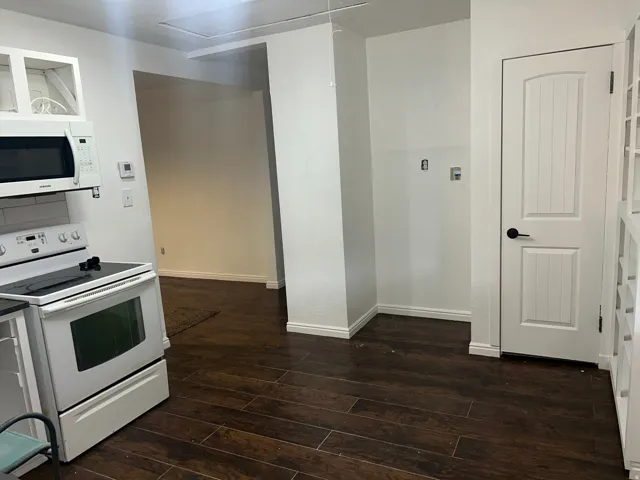 Wood-finish flooring throughout, white overhead cabinetry, and a white electric range with a microwave