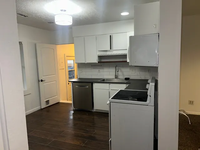 Kitchen featuring white cabinetry, dark countertops, a stainless steel dishwasher, white subway tile backsplash, and wood-finish flooring