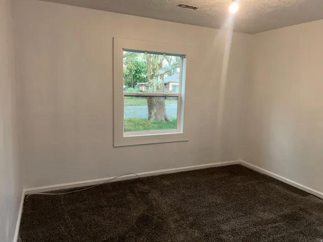 White interior walls with a single window, white trim, and dark brown carpeting