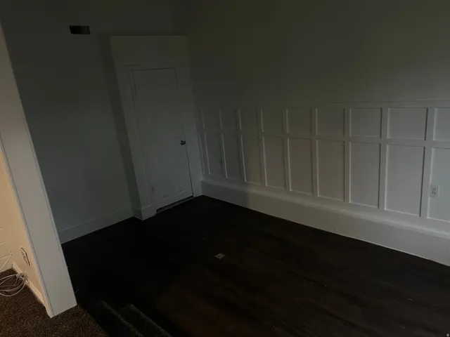 Dark wood-finish flooring, white paneled wall detailing, built-in storage, and white trim