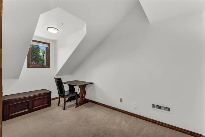 Carpeted room with sloped ceilings, a window with wood trim, and a flush-mount ceiling light fixture
