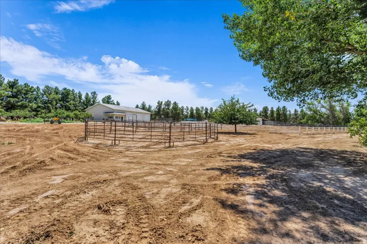 Large open lot with a metal pipe corral, a white fence line, and mature trees