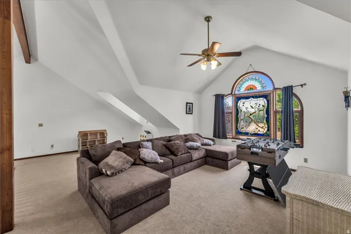Vaulted ceiling with exposed beam, arched window with stained glass, recessed wall niche, wall-mounted light fixture, and ceiling fan with integrated lighting