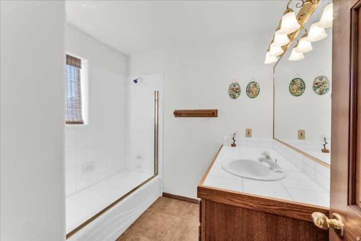 Full bathroom featuring a white tile shower surround, a built-in tub, and a vanity with a drop-in sink and a tile countertop
