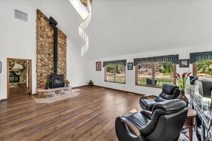 Vaulted ceiling with skylight, stone-clad fireplace with wood-burning stove, wood-finish flooring, and multiple windows with exterior access
