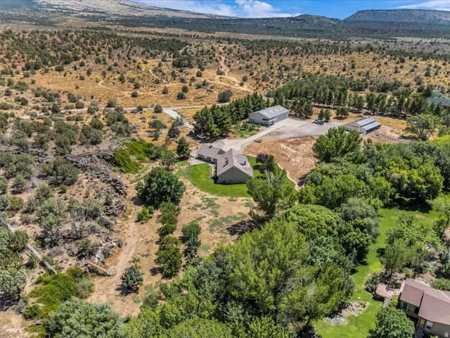 Expansive property featuring a residence with a gabled roof, multiple outbuildings, mature trees, and a vast natural landscape