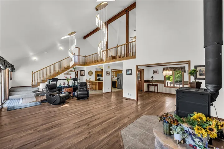 Vaulted ceilings with exposed beams, wood-finish flooring, a wood-burning stove with a tile hearth, a prominent staircase with wood railings, and a second-level open landing