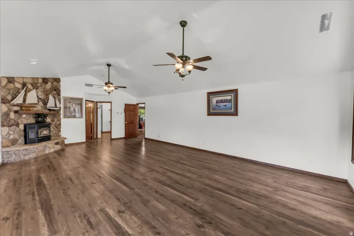 Vaulted ceilings with ceiling fans, wood-finish flooring, and a stone-clad fireplace with a wood-burning stove