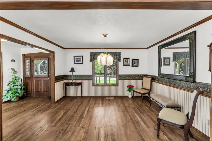 Wood-finish flooring throughout, framed window with decorative valance, elegant chandelier, wainscoting with decorative border, and a solid wood entry door with glass inserts