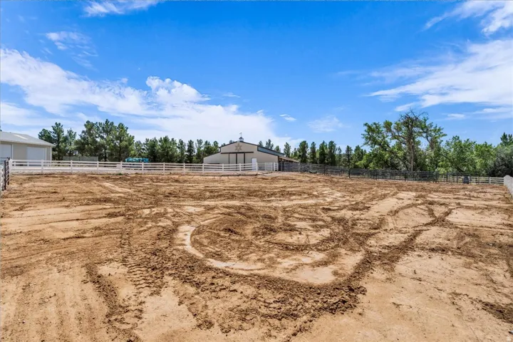 Expansive cleared lot with a white perimeter fence, mature trees, and a distant barn structure