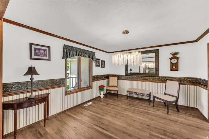 Wood-finish flooring, accent wainscoting, crown molding, and a decorative chandelier