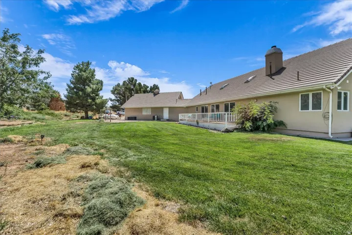 Expansive green lawn, tiled roof, multiple skylights, stucco exterior, and a rear deck with white railing