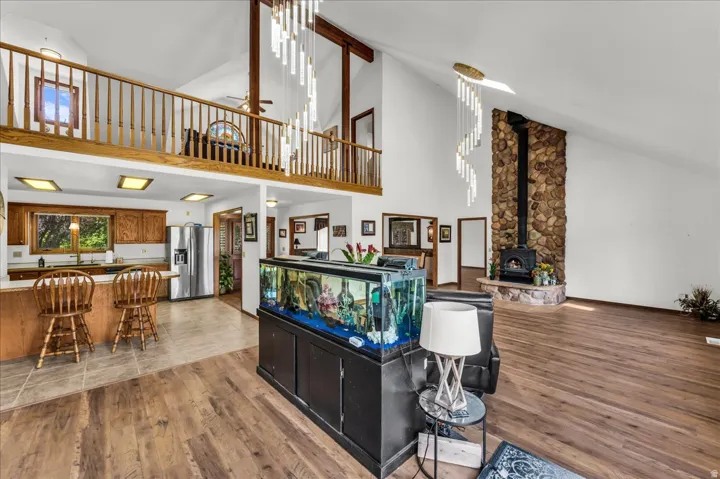 Vaulted ceilings, wood-finish flooring, stone-faced fireplace with wood-burning stove, open-concept kitchen with wood cabinetry and stainless steel appliances, and a second-level open balcony