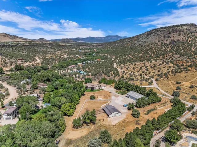 Expansive property featuring multiple structures, mature trees, a large unpaved parking area, and distant mountain backdrops