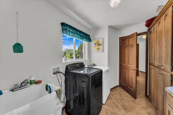 Utility room featuring a window, built-in storage cabinetry, a utility sink, and tile flooring