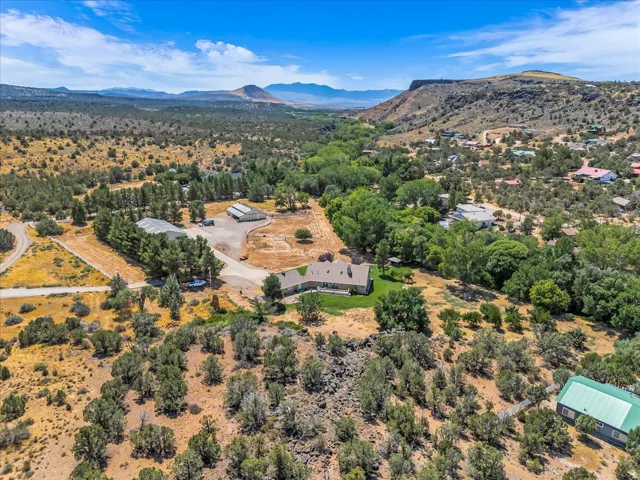 Expansive property featuring a central residence, multiple accessory structures, mature trees, and natural desert landscaping