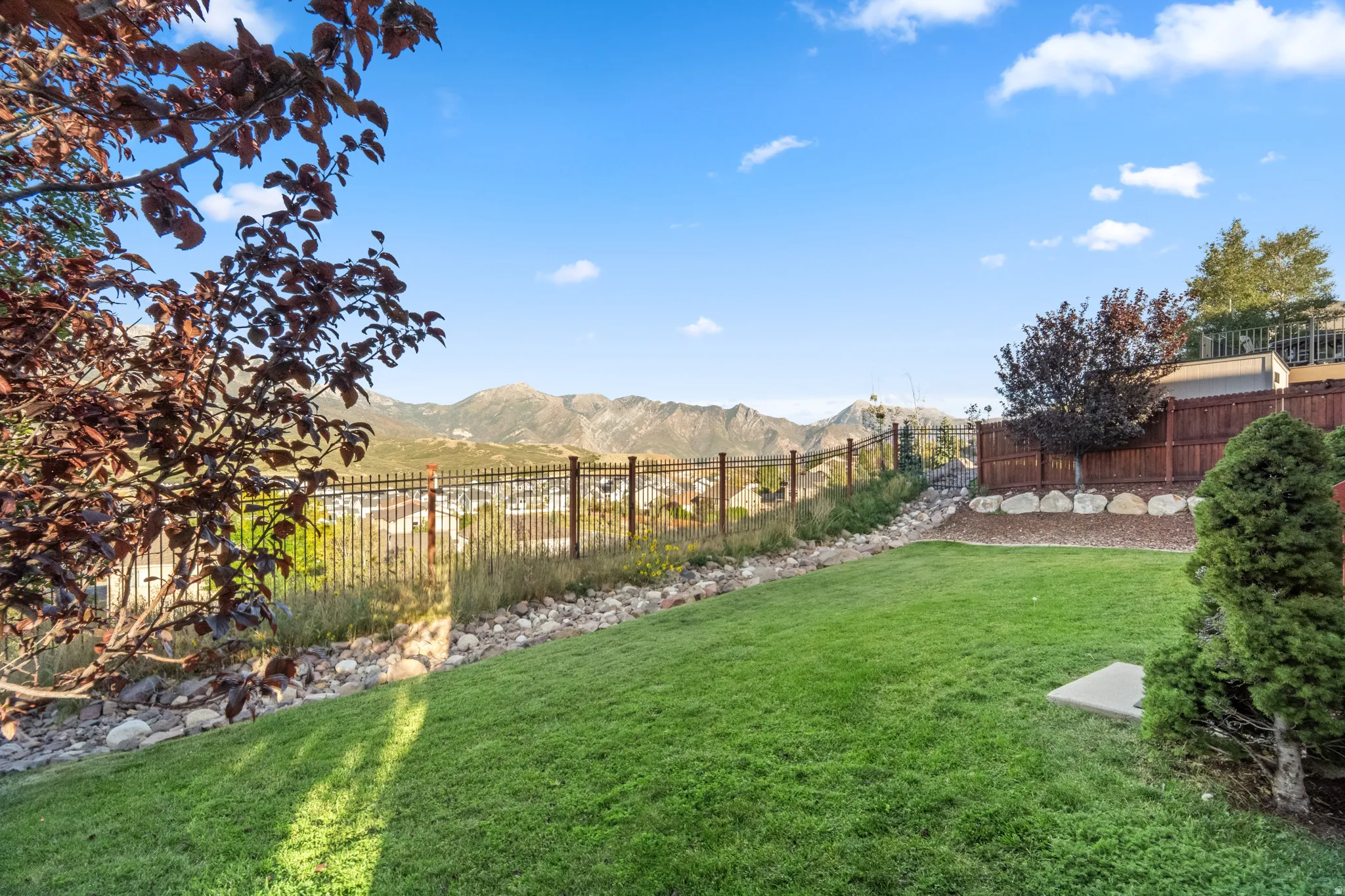 Expansive lawn area with a black metal fence, bordered by natural rock landscaping, and mature trees