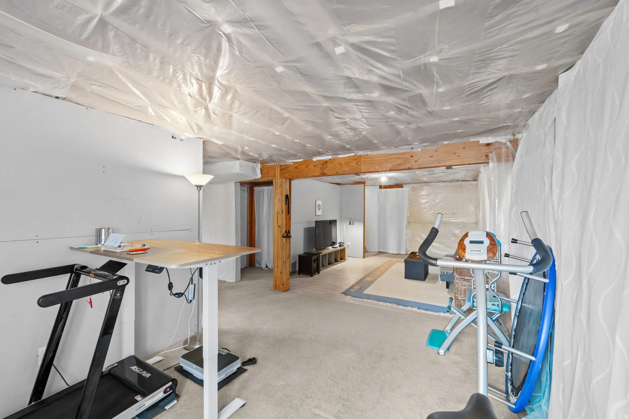 Unfinished basement space with exposed wood beams, carpeted flooring, and partial wall coverings