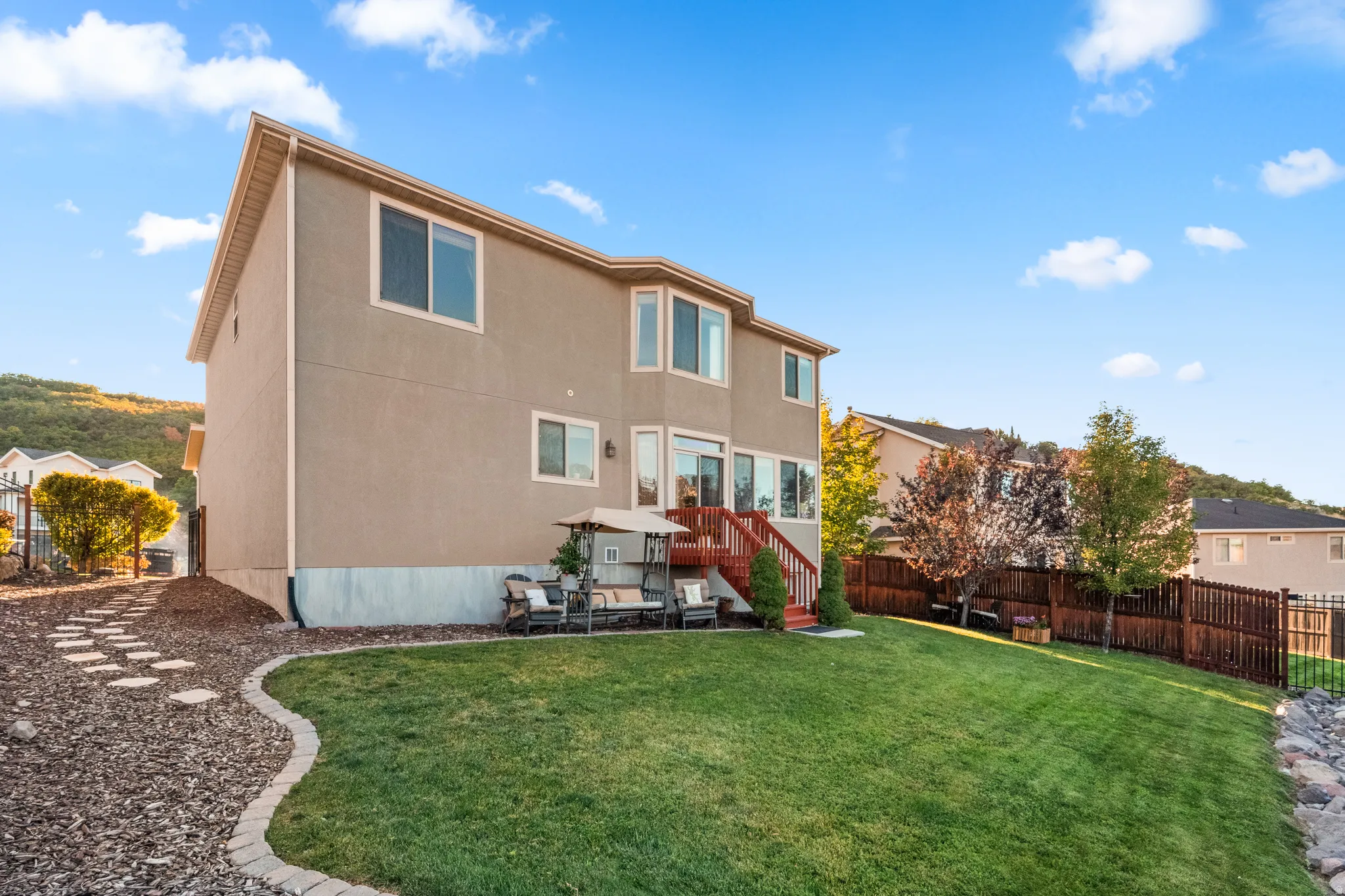 Expansive backyard featuring a manicured lawn, multi-level wood deck, stone-edged garden beds, and a perimeter fence