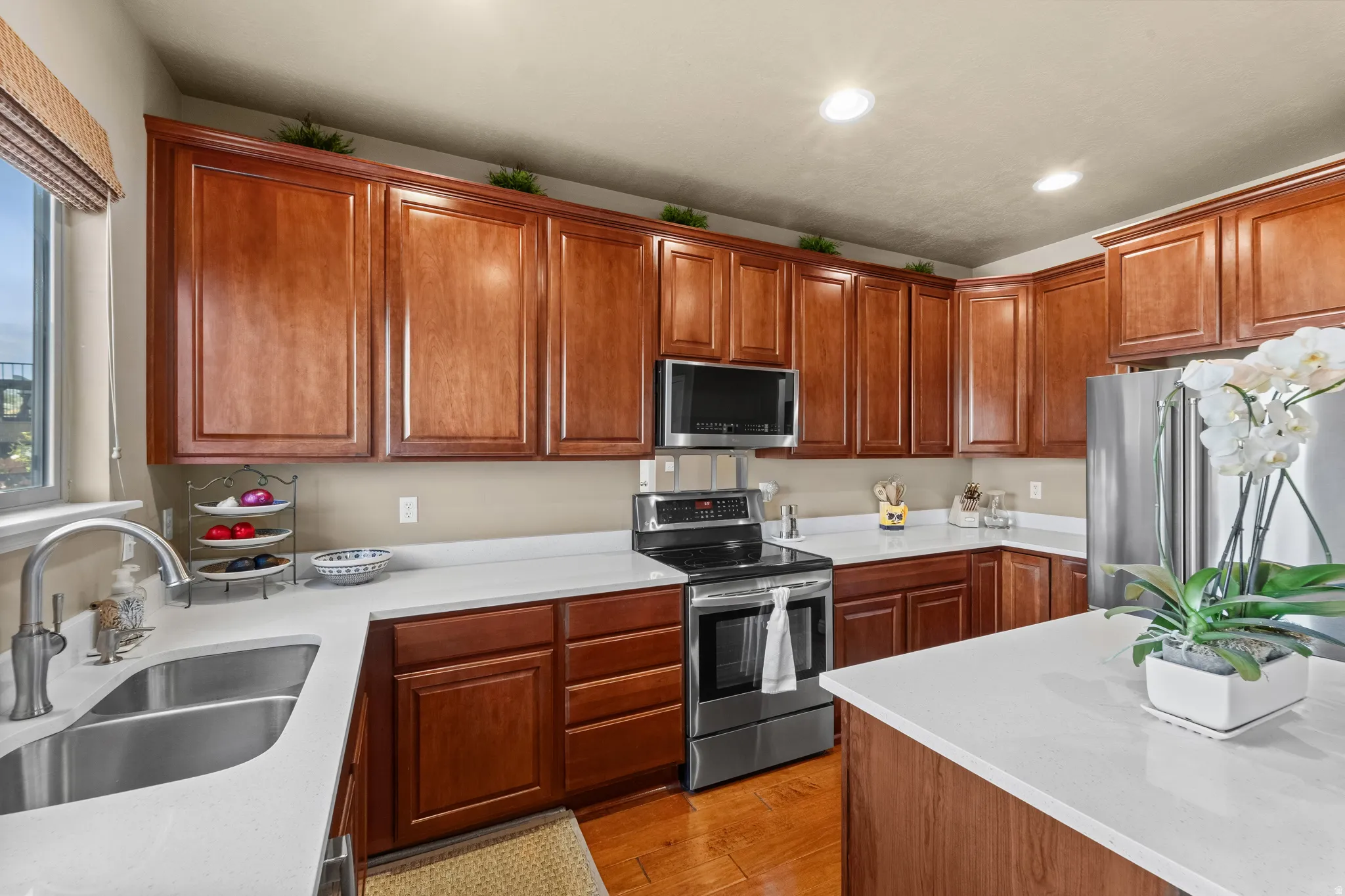 Kitchen featuring wood-finish cabinetry, stainless steel appliances, white countertops, a double basin sink, and recessed lighting