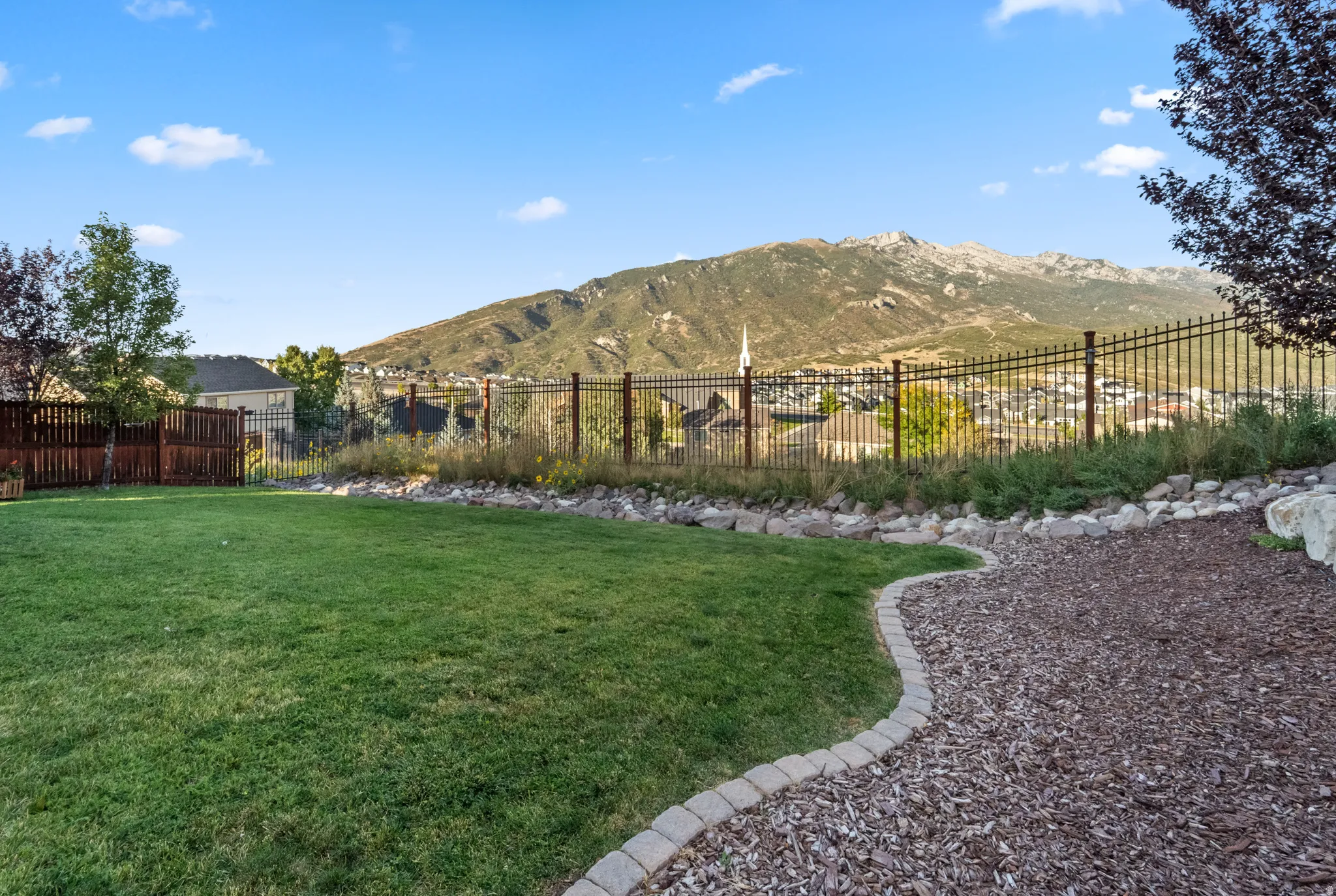 Expansive lawn area with a decorative bark path, bordered by a retaining wall and an ornamental metal fence