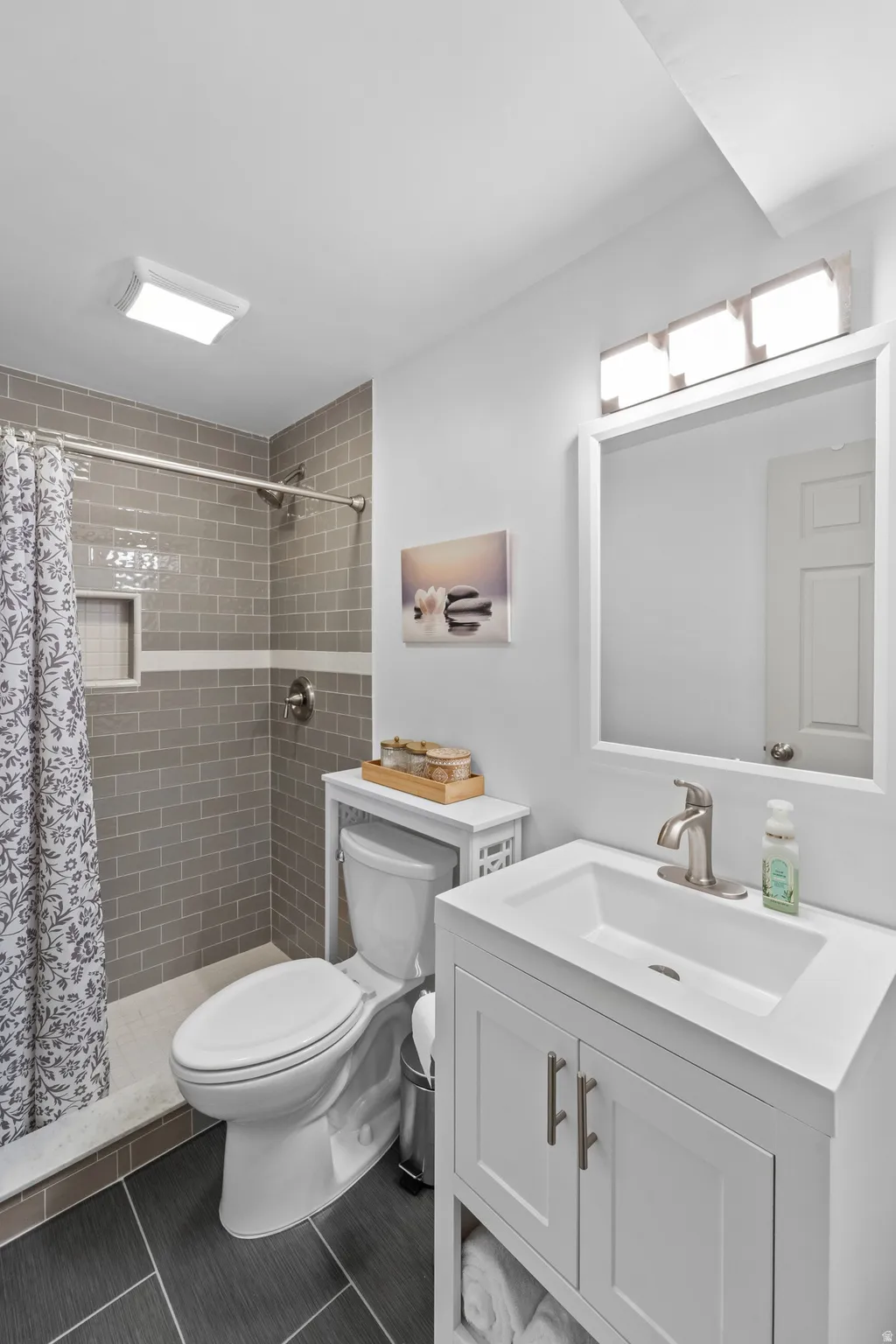 Common bathroom - Shower with subway tile surround, single-basin vanity with storage, and dark tile flooring