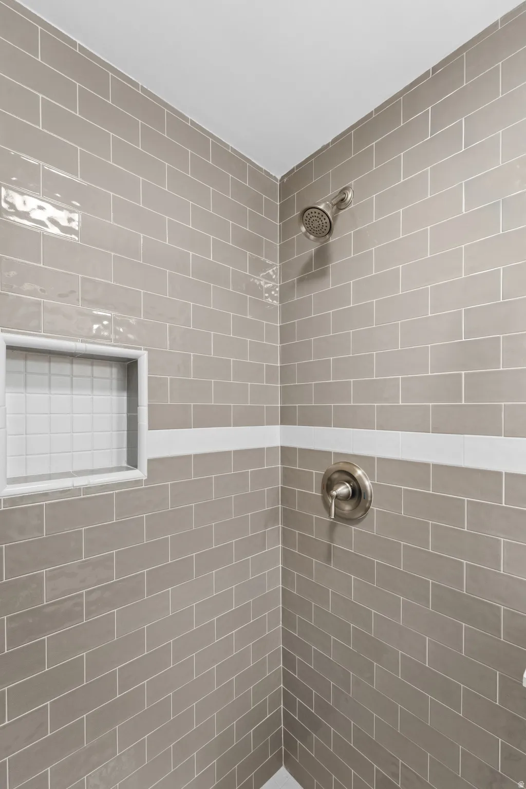 Finished basement Shower featuring gray subway tile, a recessed niche with white square tile, and brushed nickel fixtures