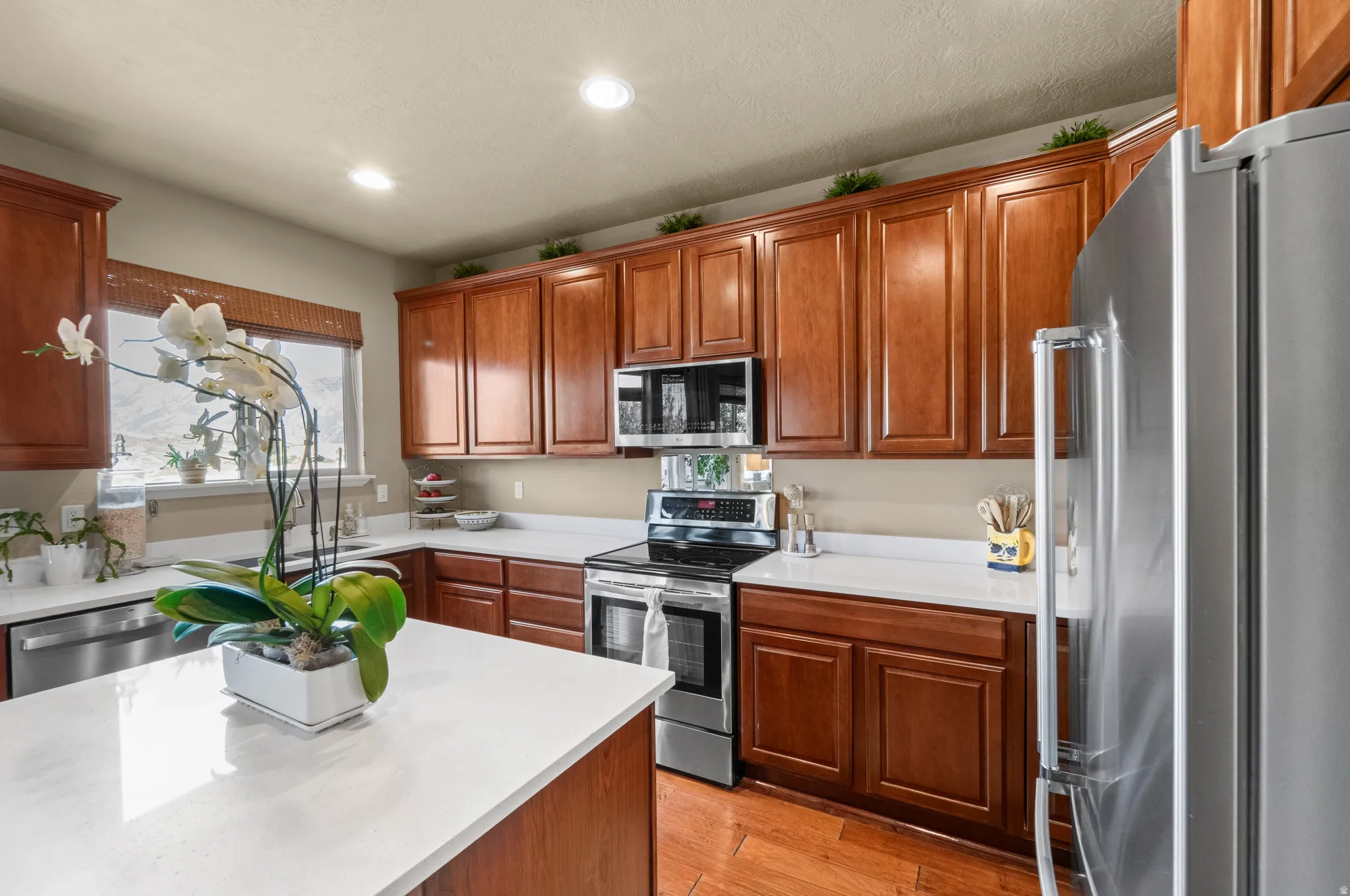 Kitchen featuring wood-finish flooring, recessed lighting, wood cabinetry, stainless steel appliances, and white countertops