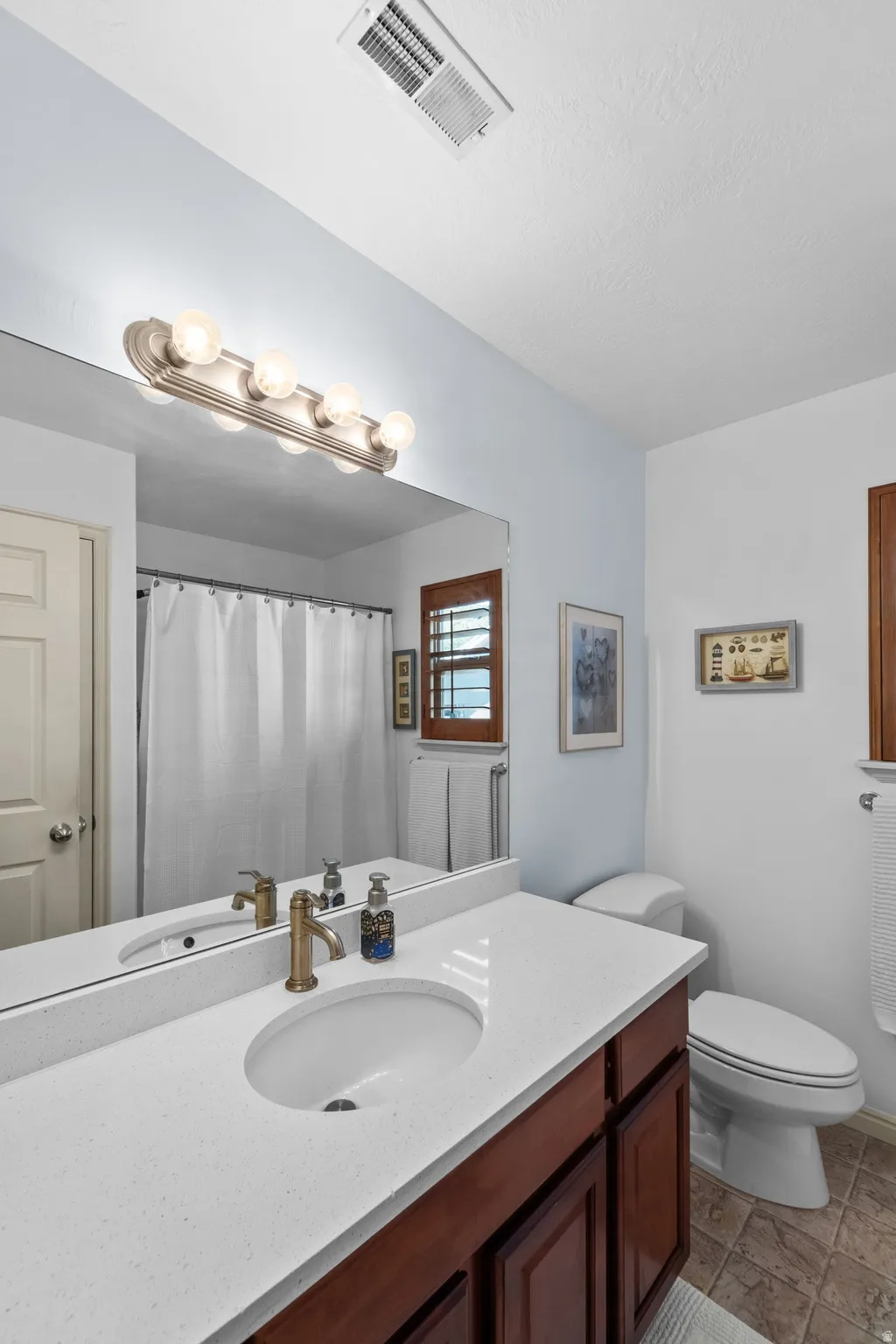Vanity with a white countertop and integrated sink, bronze-finish faucet, and wood-finish cabinetry