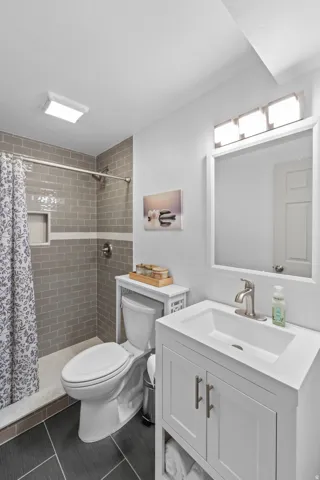 Common bathroom - Shower with subway tile surround, single-basin vanity with storage, and dark tile flooring