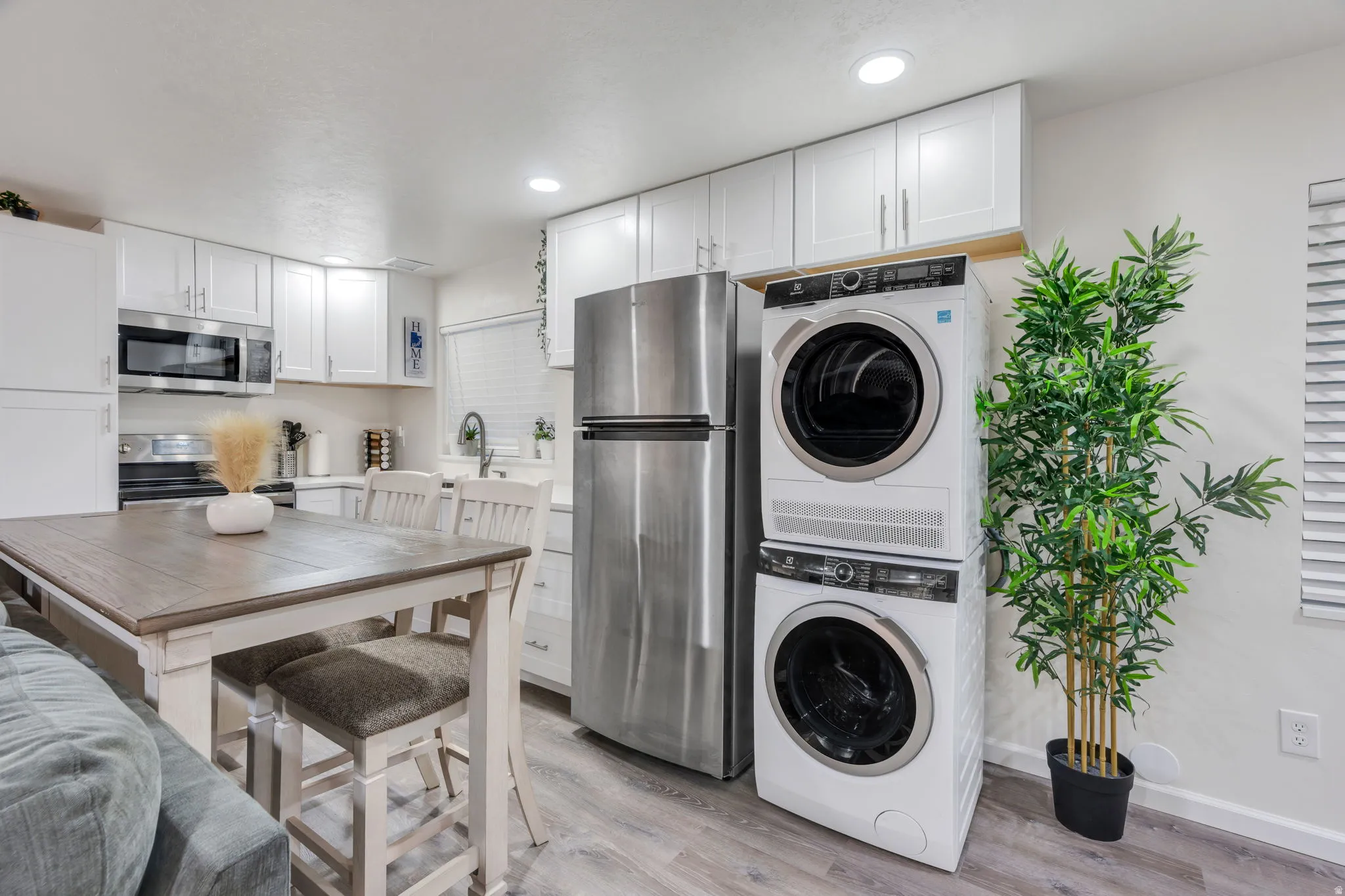 White shaker cabinetry, stainless steel appliances, wood-finish flooring, stacked laundry appliances, recessed lighting