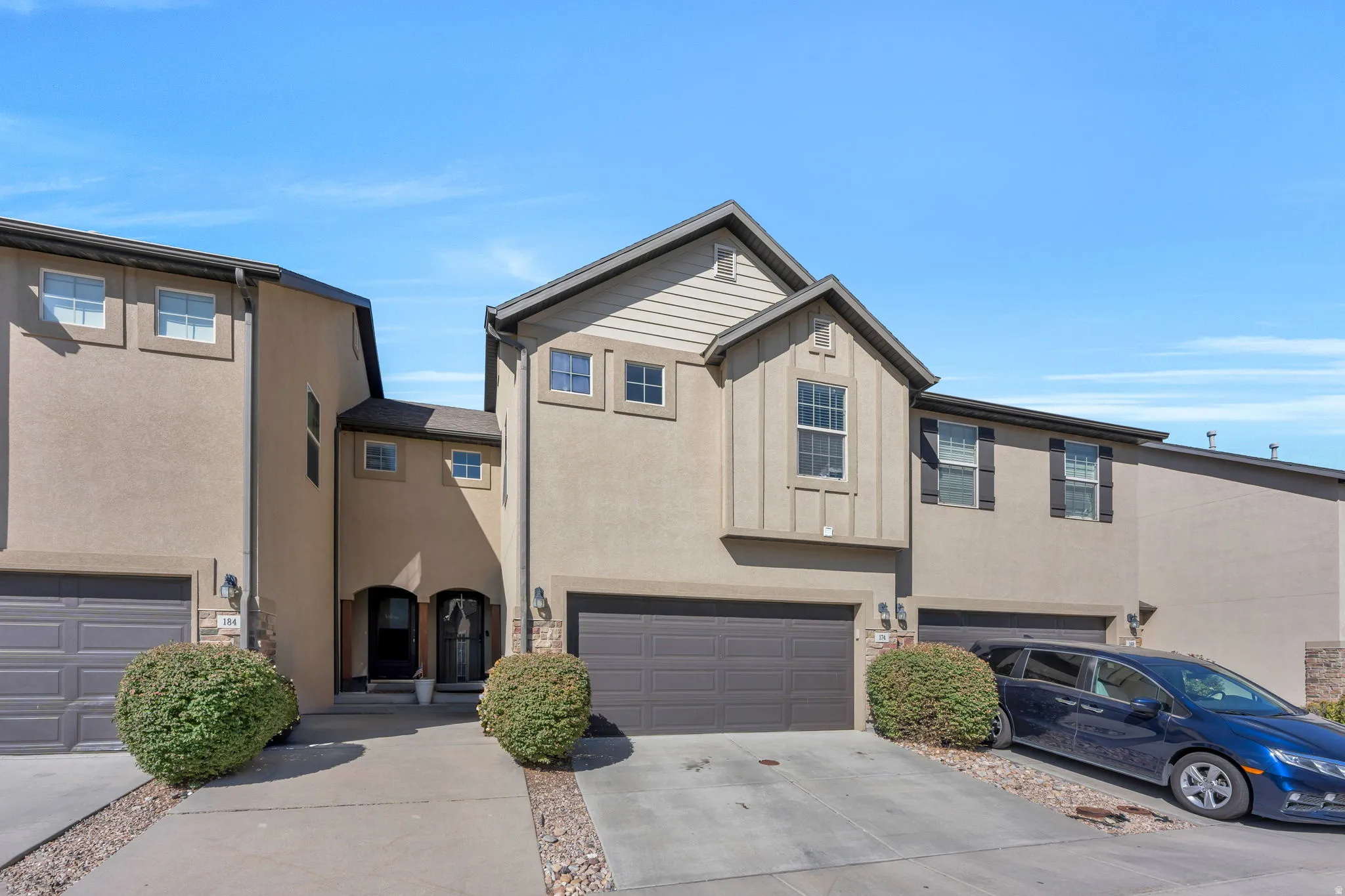 Exterior stucco finish, attached two-car garage, multiple windows with dark shutters, prominent gabled architectural feature, and a paved driveway
