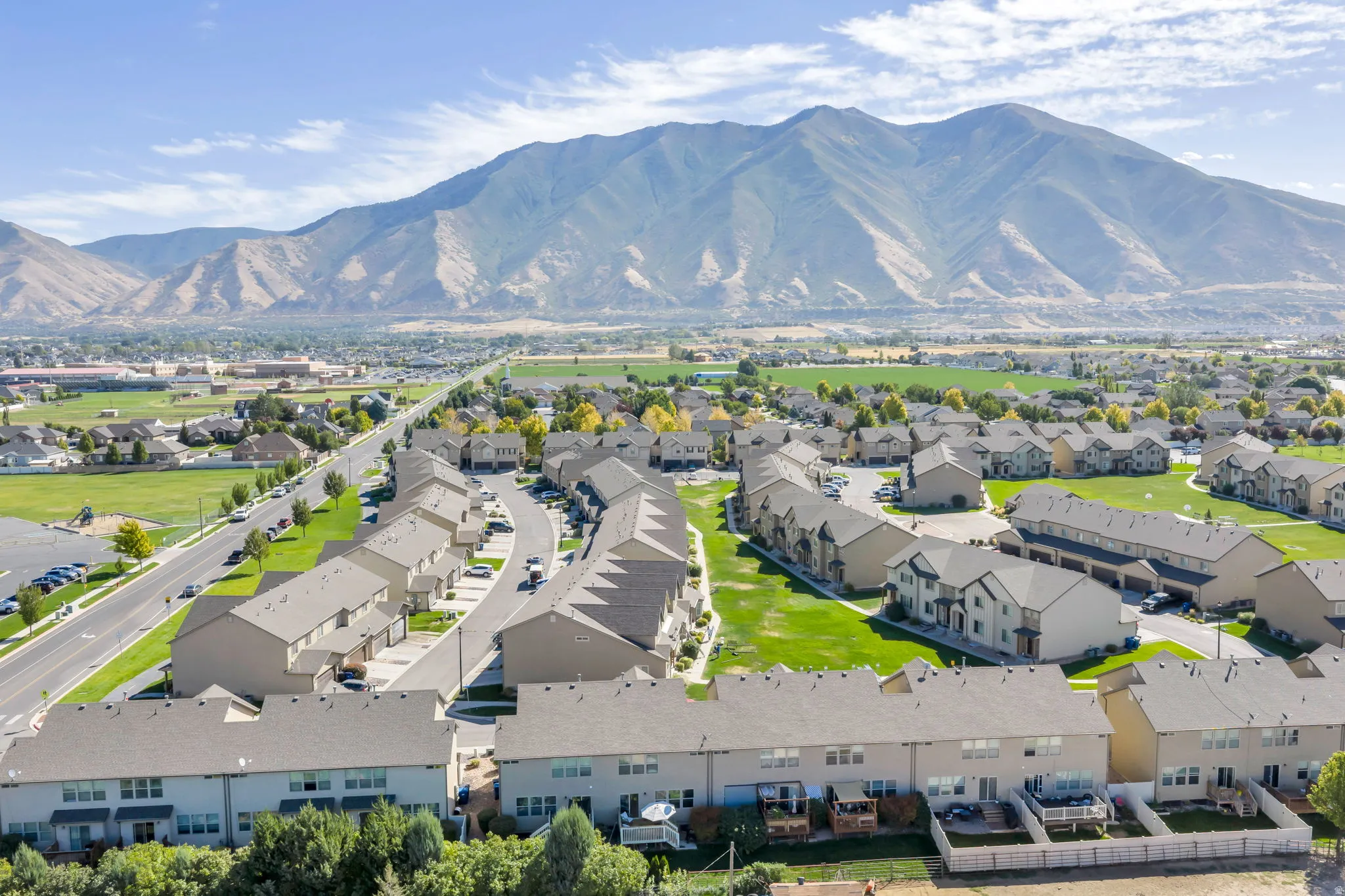 Expansive mountain backdrop with a residential community featuring townhomes, green spaces, and paved roads