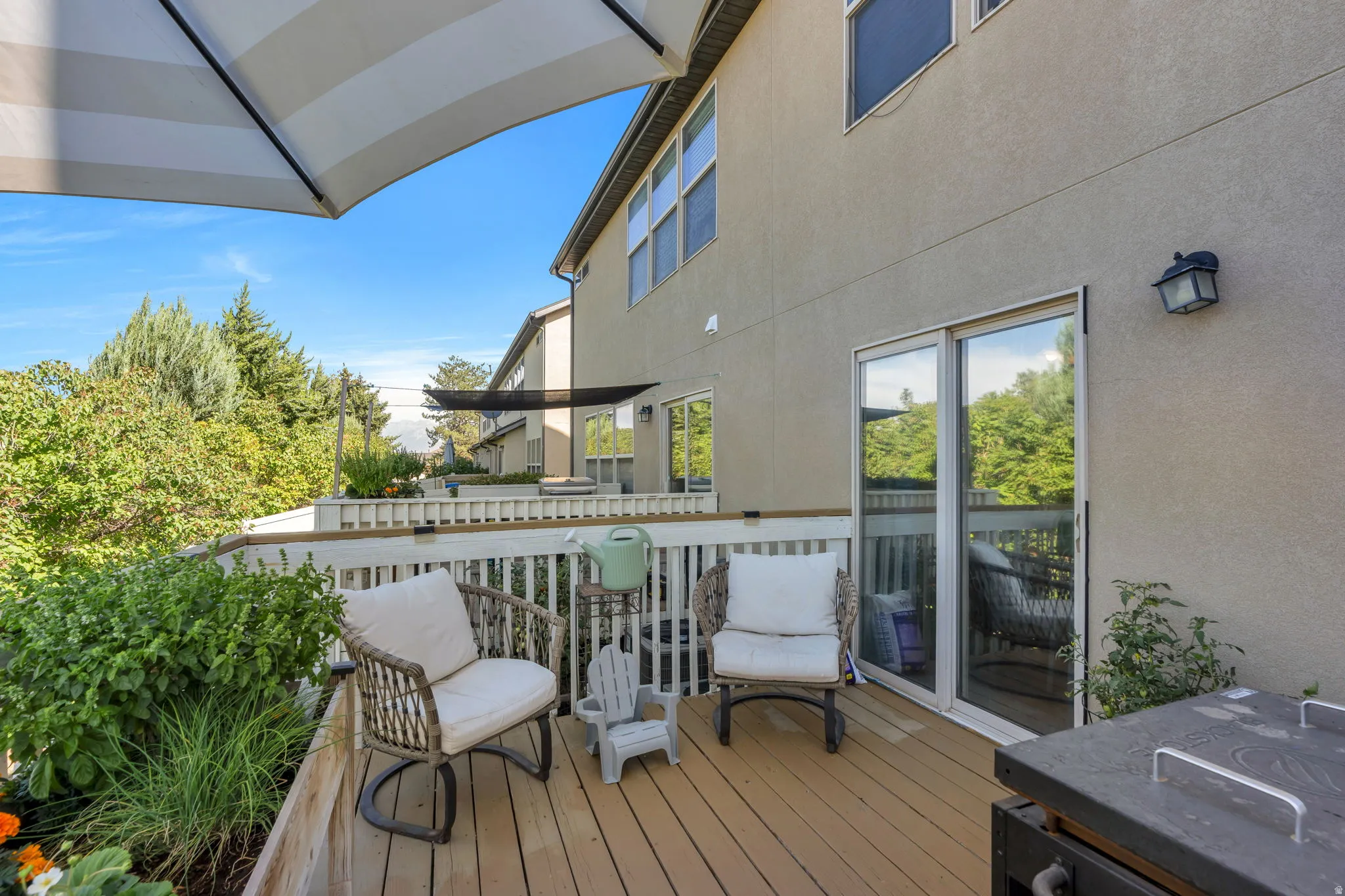 Expansive wooden deck with a white railing system, featuring multiple windows and a sliding glass door on the stucco exterior