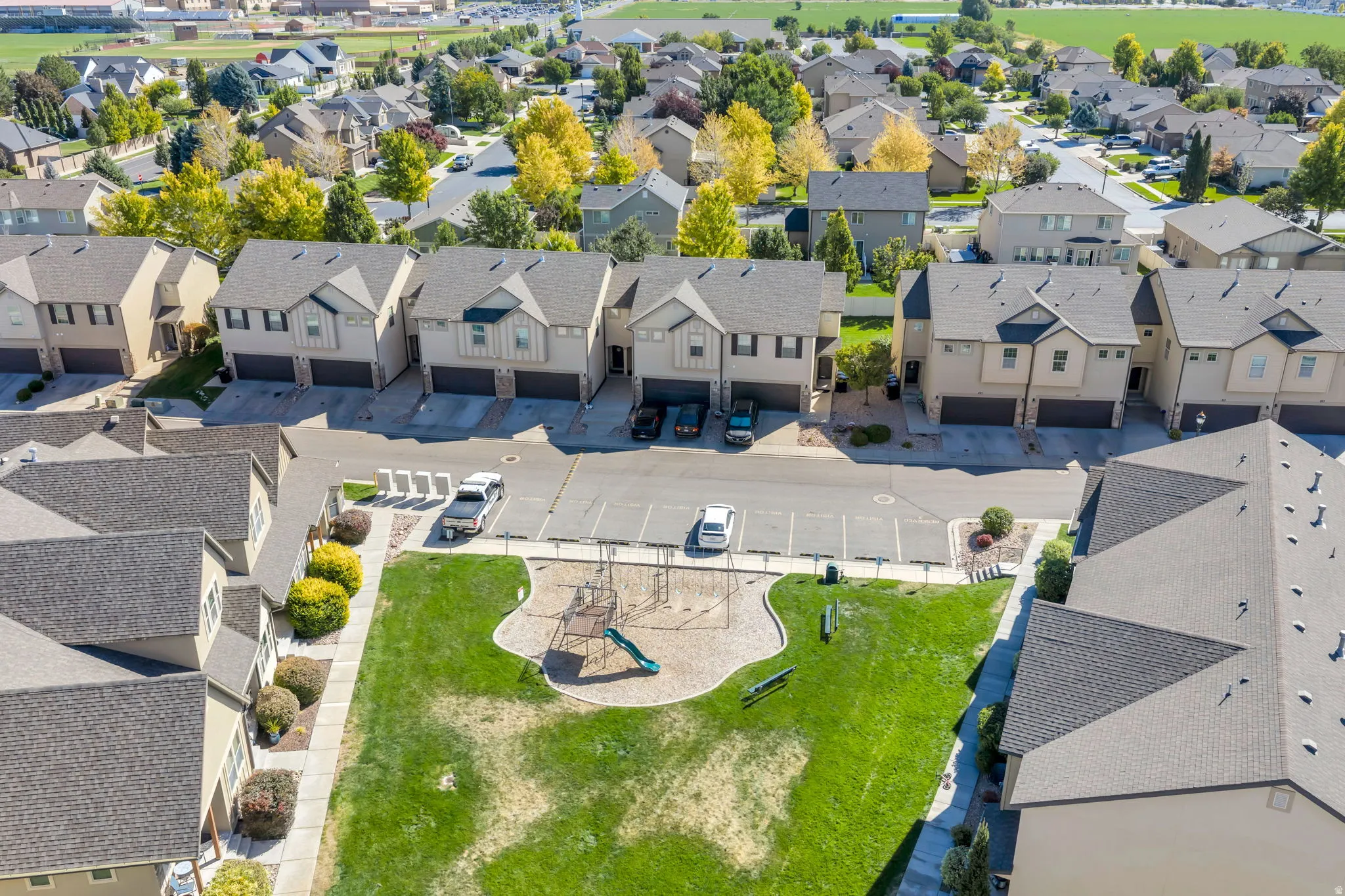 Townhome community featuring private garages, paved driveways, a common green space, and a playground