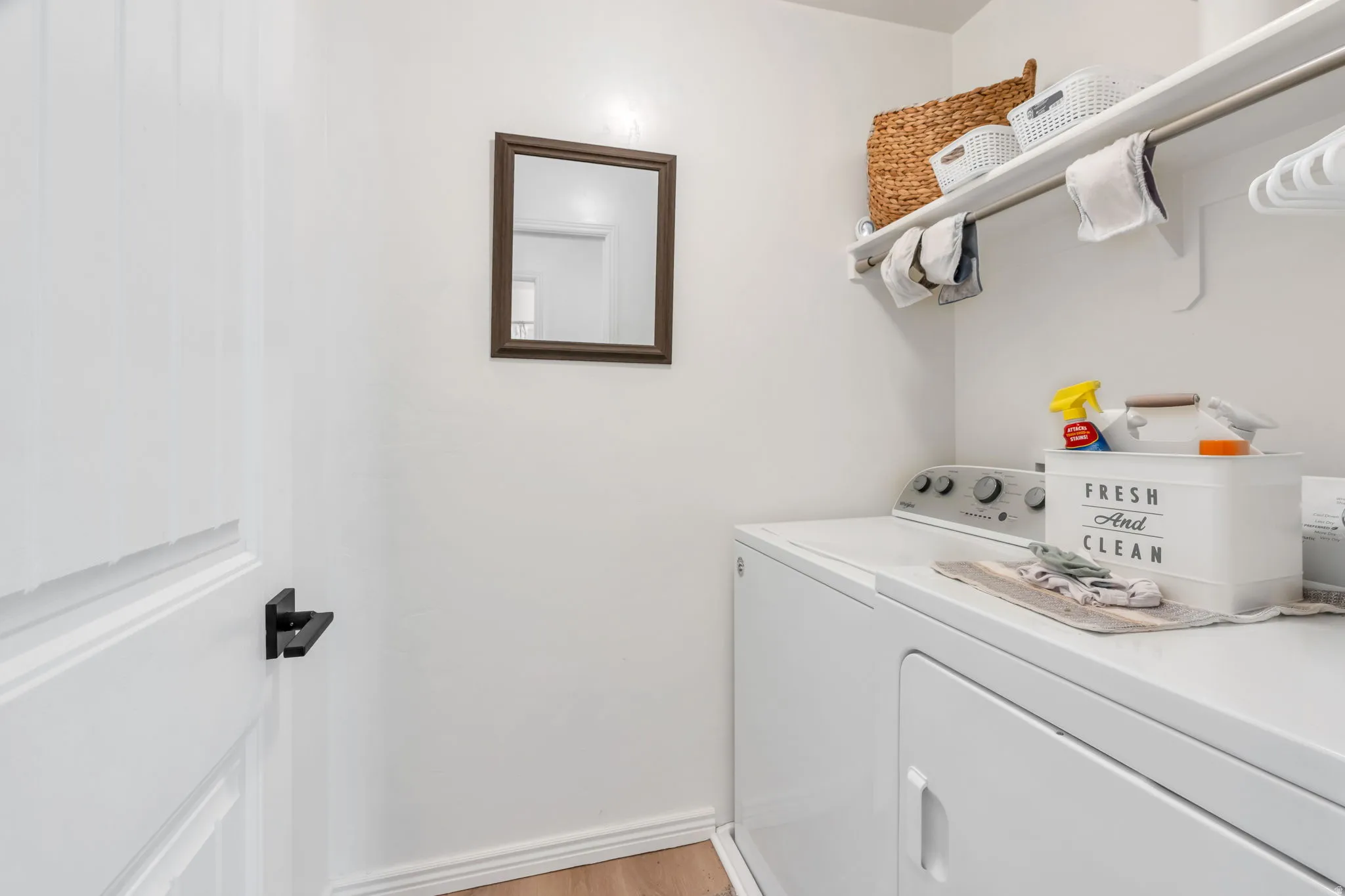 Dedicated laundry area featuring white walls, open shelving, a metal hanging rod, and light wood-finish flooring