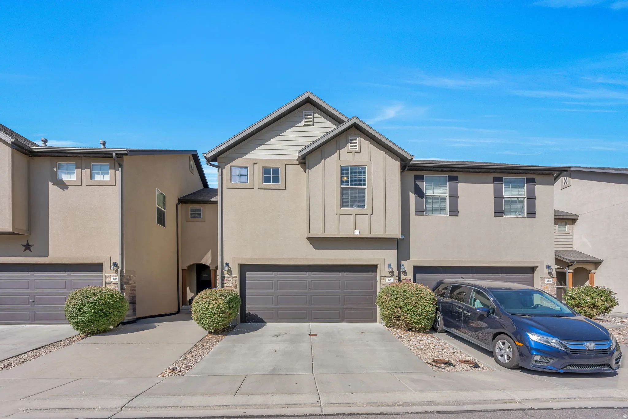 Townhome exterior featuring stucco siding, stone accents, two-car garage, and a peaked roofline