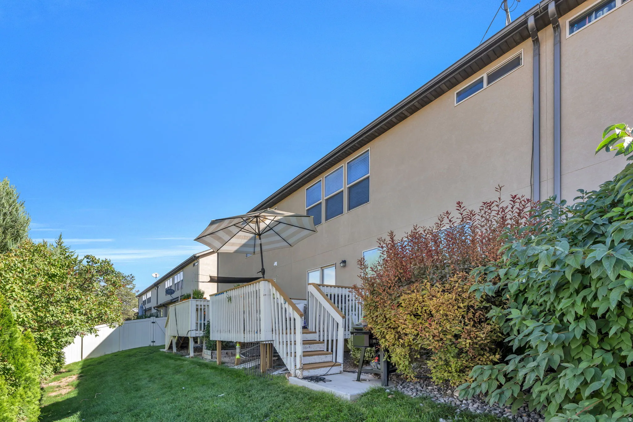 Expansive backyard featuring a manicured lawn, dedicated patio space, wood deck with stairs, mature landscaping, and a stucco exterior