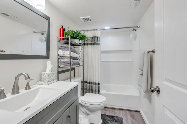 Vanity with integrated sink, rectangular mirror, brushed nickel fixtures, tub and shower combination, and wood-finish flooring