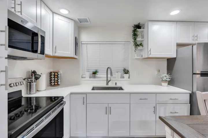 White cabinetry with chrome hardware, stainless steel appliances, a stainless steel sink with a gooseneck faucet, and light-toned countertops