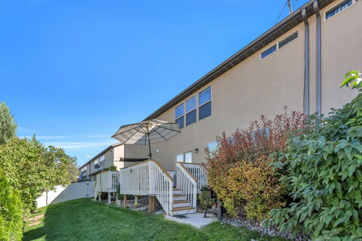Expansive backyard featuring a manicured lawn, dedicated patio space, wood deck with stairs, mature landscaping, and a stucco exterior