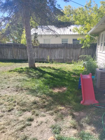 Private backyard featuring a wooden privacy fence, mature trees, and a visible air conditioning unit